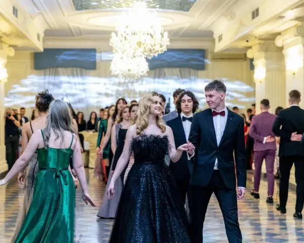 Młoda para w eleganckich strojach, ona w czarnej sukni, on w garniturze, idzie na bal studniówkowy.