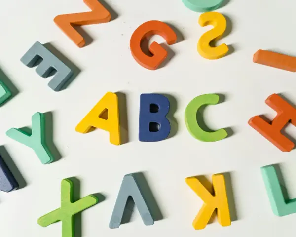 Kolorowe drewniane litery, idealne dla nauczyciela wychowania przedszkolnego, tworzą napis "ABC" i inne znaki.