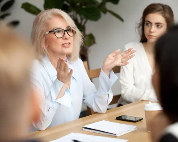Kobieta w okularach gestykuluje, prowadząc dyskusję podczas rady pedagogicznej.