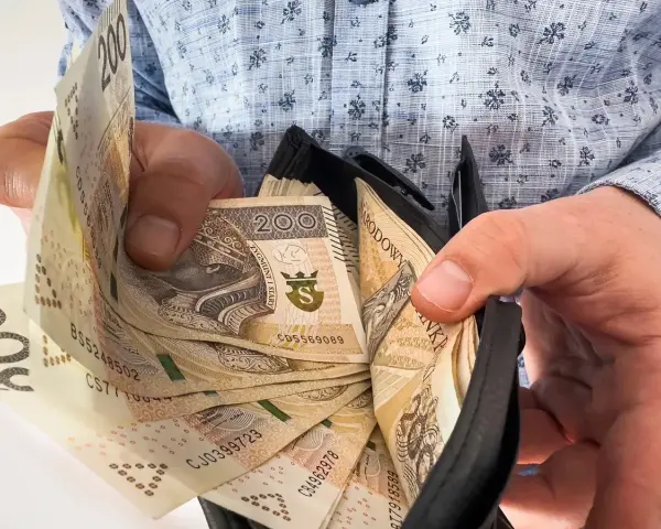 Ręce trzymają portfel z banknotami 200 zł. To symboliczne przedstawienie nagrody jubileuszowej za 15 lat pracy.
