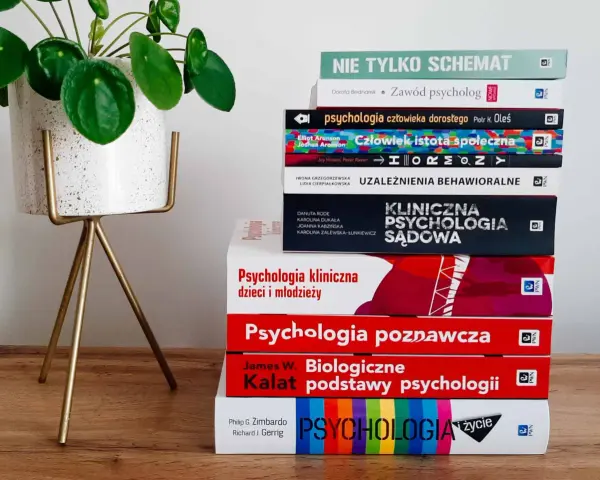Stos książek o psychologii, od ogólnych po specjalistyczne, sugeruje, ile trwają studia psychologiczne. Obok zielona roślina.