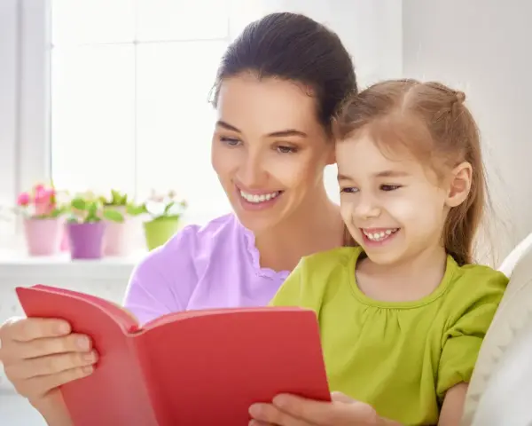 Uśmiechnięta mama czyta bajkę córce. To wspaniała opieka na dziecko 2 dni w tygodniu, pełna radości i wspólnych chwil.