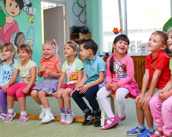 Uśmiechnięte dzieci siedzą w przedszkolu. Od ilu lat można tu uczęszczać?