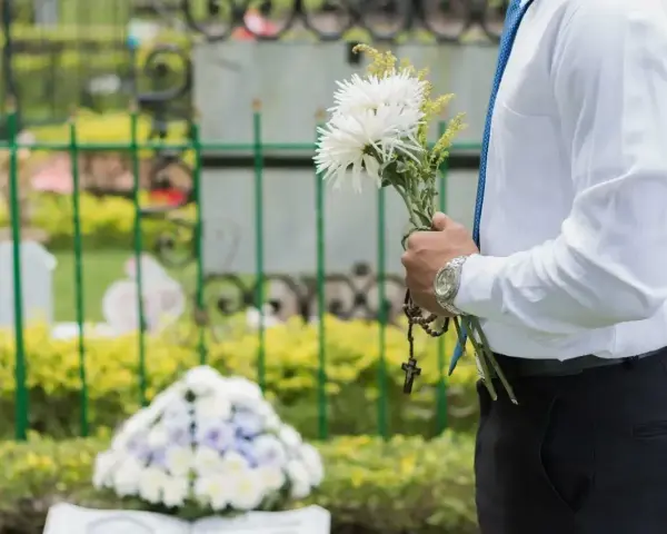 Mężczyzna w białej koszuli i niebieskim krawacie trzyma bukiet białych kwiatów i różaniec. To jego urlop okolicznościowy śmierć teścia.