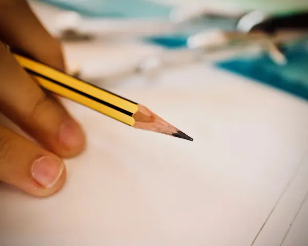 Dłoń trzymająca ołówek nad kartką papieru, symbol wsparcia w edukacji, w tym dla osób ze specjalnymi potrzebami edukacyjnymi.