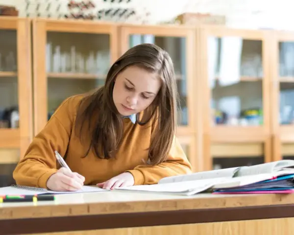 Dziewczyna pisze w zeszycie, przygotowując się do egzaminu. Marzy o stypendium szkolnym, które pomoże jej w dalszej nauce.