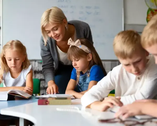 Uśmiechnięta nauczycielka wspiera dzieci w nauce. To praca, którą wykonuje oligofrenopedagog, pomagając maluchom rozwijać się.