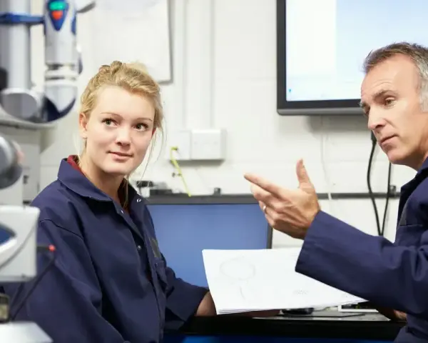 Młoda pracownica i starszy mężczyzna omawiają dokumentację techniczną. To część rutynowych badań okresowych pracowników.