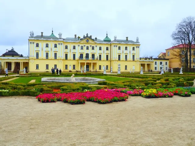 Pałac Branickich, siedziba Uniwersytetu Medycznego w Białymstoku, otoczony barokowym ogrodem z fontanną i kwitnącymi rabatami.