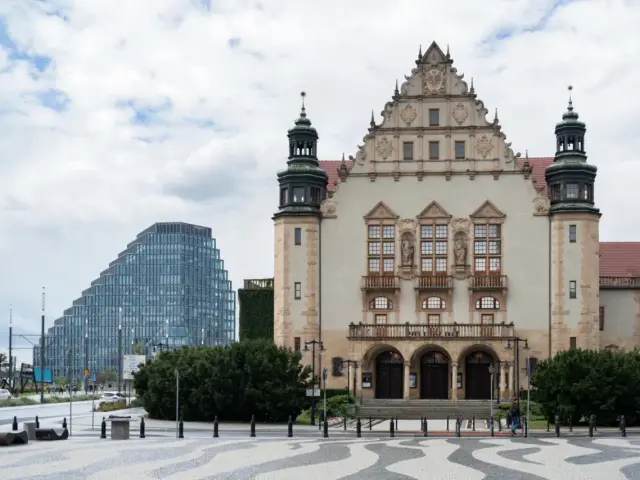 Imponujący budynek **Uniwersytetu im. Adama Mickiewicza w Poznaniu** obok nowoczesnego wieżowca.