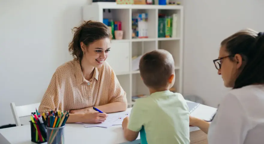 Uśmiechnięta nauczycielka omawia z rodzicami orzeczenie o potrzebie kształcenia specjalnego dla dziecka.