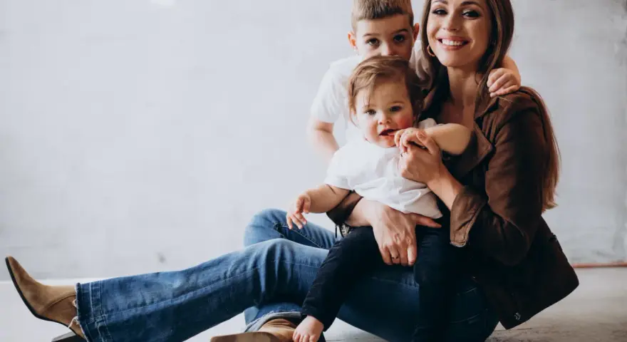 Szczęśliwa mama z dwójką dzieci, maluszkiem na rękach i starszym synkiem za plecami. Idealny urlop na dziecko.