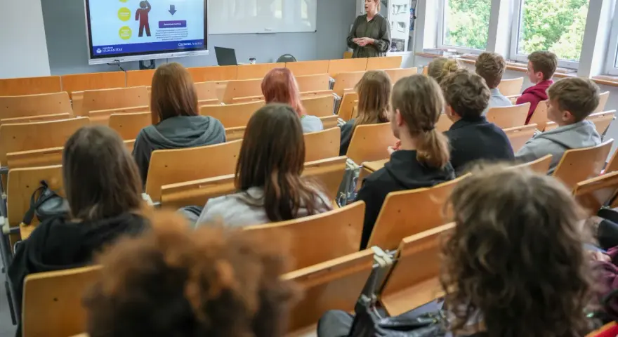 Wykład o przygotowaniu pedagogicznym dla psychologów. Studenci słuchają prelegentki przy tablicy interaktywnej.