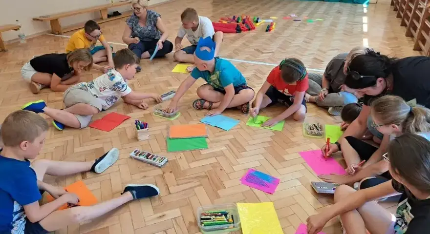 Dzieci klas 1-3 biorą udział w zabawach integracyjnych, rysując na kolorowych kartkach.