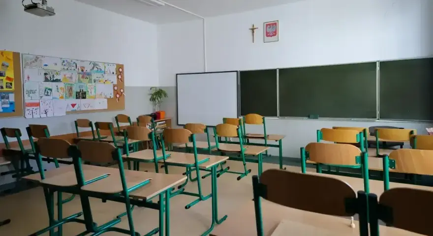 Pusta klasa szkolna z ławkami i krzesłami. Na ścianie tablica, projektor i dziecięce rysunki. Dziś odwołane zajęcia w szkołach.