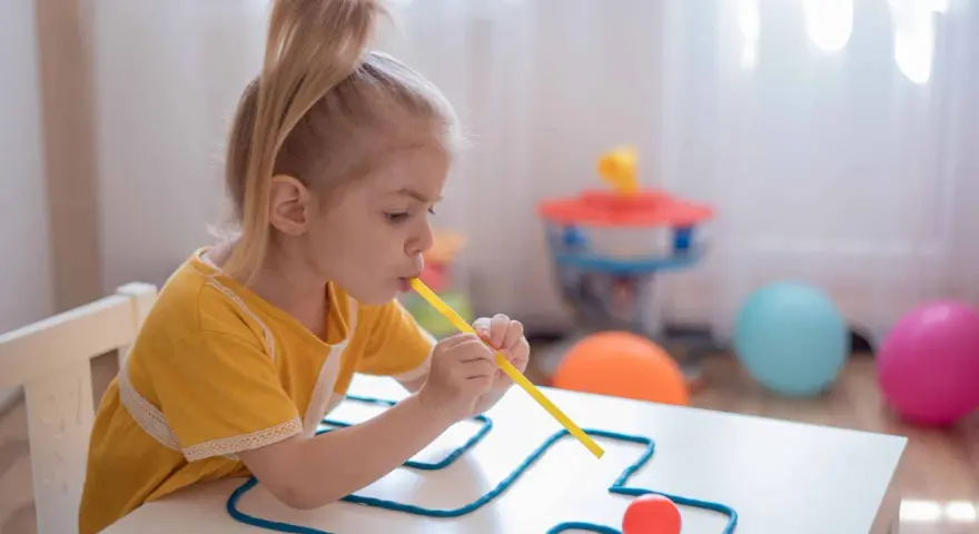 Dziewczynka ćwiczy mowę, dmuchając przez słomkę, co jest częścią terapii na dyslalię wieloraką.