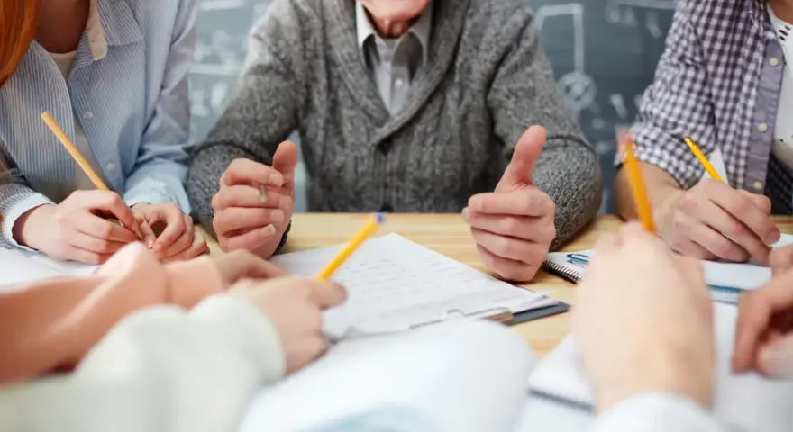 Uśmiechnięty nauczyciel w stanie nieczynnym, otoczony przez studentów piszących notatki.
