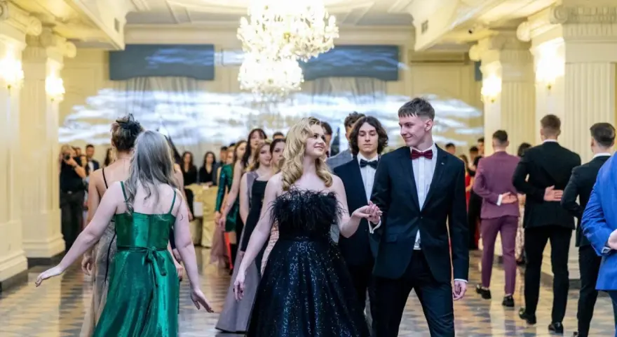 Młoda para w eleganckich strojach, ona w czarnej sukni, on w garniturze, idzie na bal studniówkowy.
