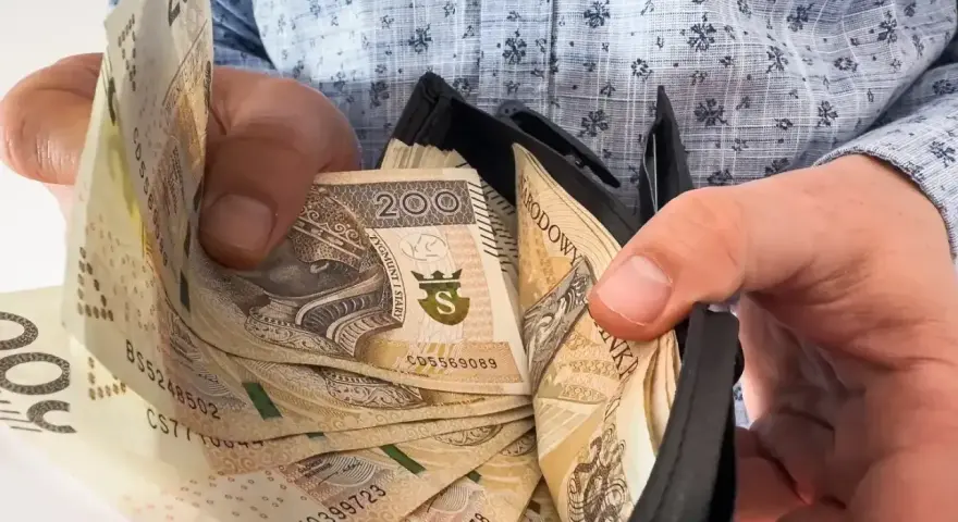 Ręce trzymają portfel z banknotami 200 zł. To symbol nagrody jubileuszowej za 40 lat pracy w budżetówce.