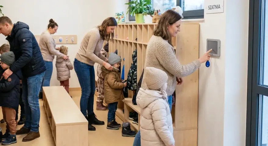 Rodzice z dziećmi w szatni, przygotowujący się do wyjścia. System kontroli zarządczej ułatwia zarządzanie wejściami i wyjściami.
