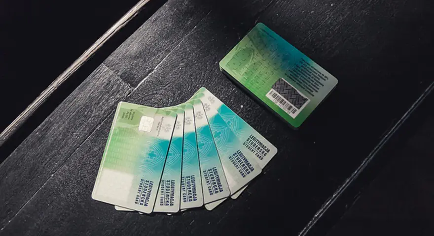 Kilka zielonych legitymacji studenckich leży na ciemnej powierzchni.