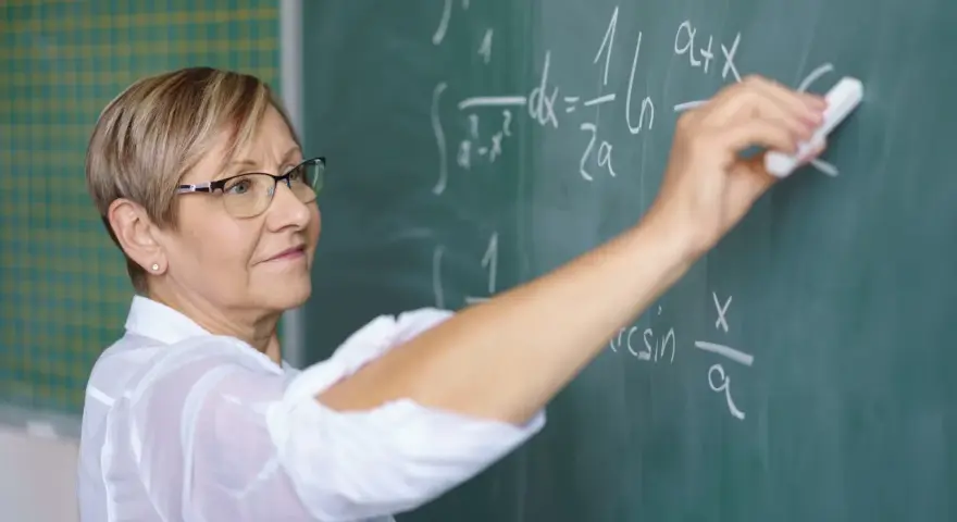 Nauczycielka matematyki pisze na tablicy wzory. Czy to zapowiedź podwyżki dla nauczycieli? Najnowsze wiadomości.