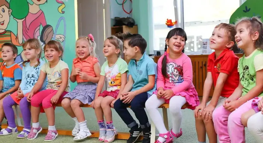 Uśmiechnięte dzieci siedzą w przedszkolu. Od ilu lat można tu uczęszczać?