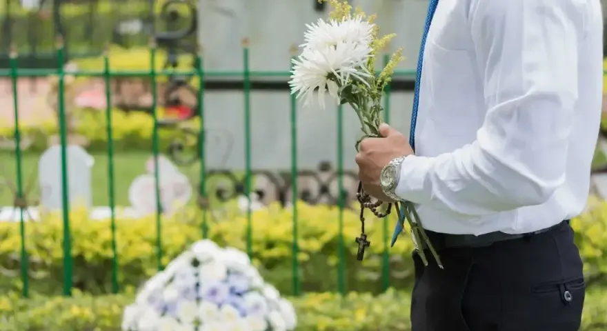Mężczyzna w białej koszuli i niebieskim krawacie trzyma bukiet białych kwiatów i różaniec. To jego urlop okolicznościowy śmierć teścia.