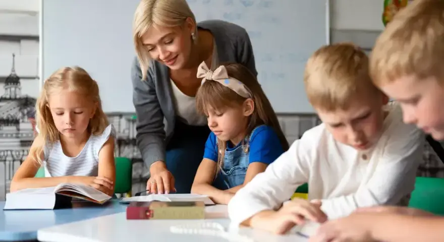 Uśmiechnięta nauczycielka wspiera dzieci w nauce. To praca, którą wykonuje oligofrenopedagog, pomagając maluchom rozwijać się.