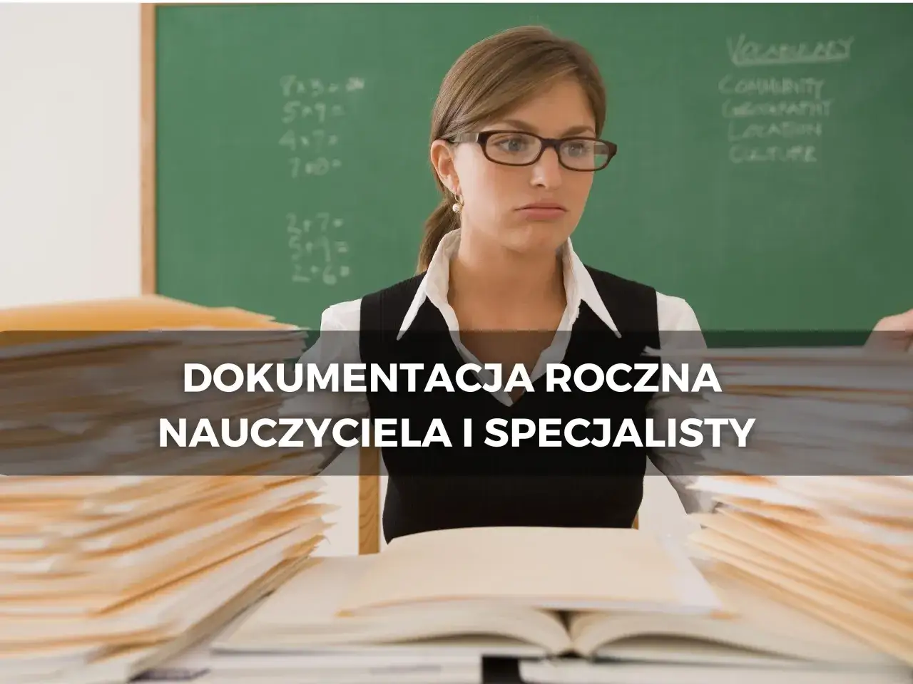 Nauczycielka w okularach przy biurku pełnym dokumentów. Na tablicy matematyczne zadania i słówka. To obraz związany z mianowaniem i dokumentacją roczną.
