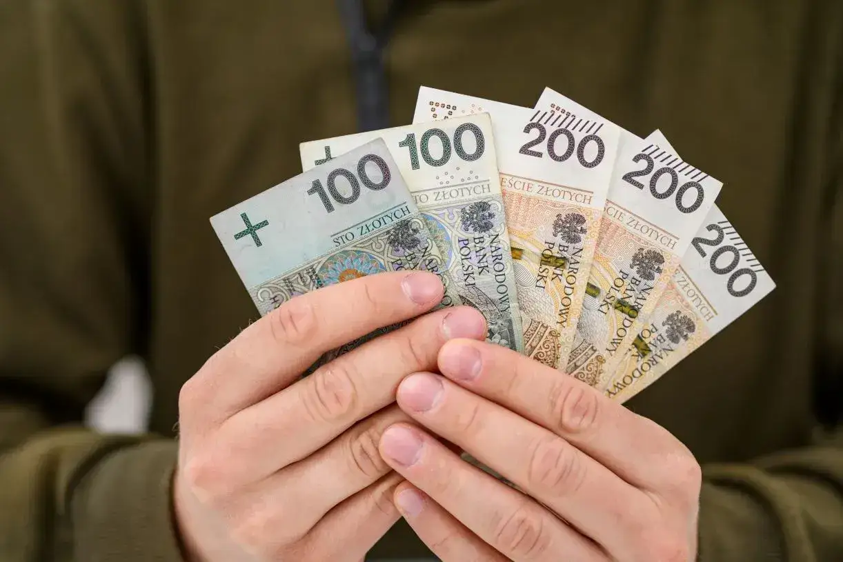 Dłonie trzymają polskie banknoty: dwie stówy i trzy dwusetki. Symbolizują one oczekiwane podwyżki dla pracowników samorządowych.