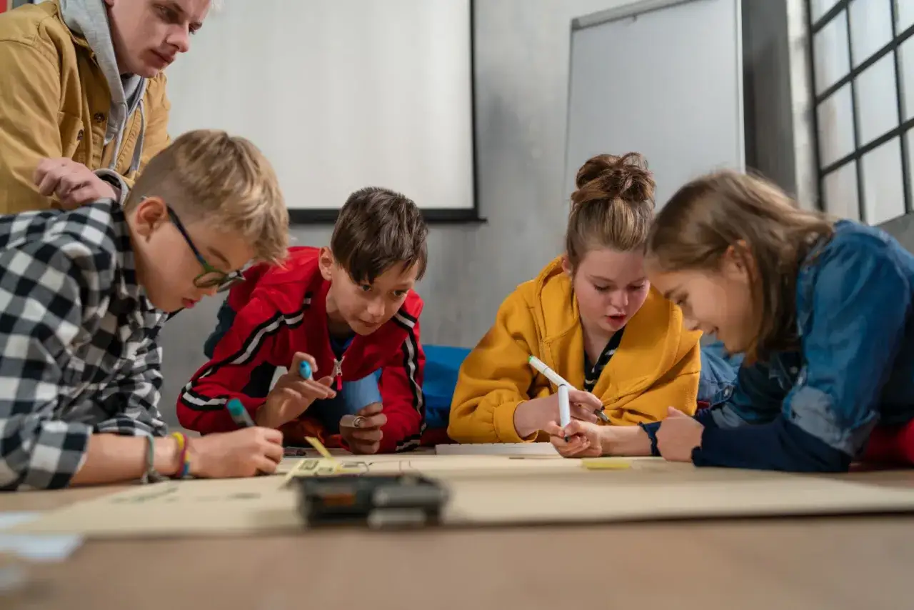Dzieci i młody mężczyzna pracują razem nad projektem, ćwicząc umiejętności społeczne.