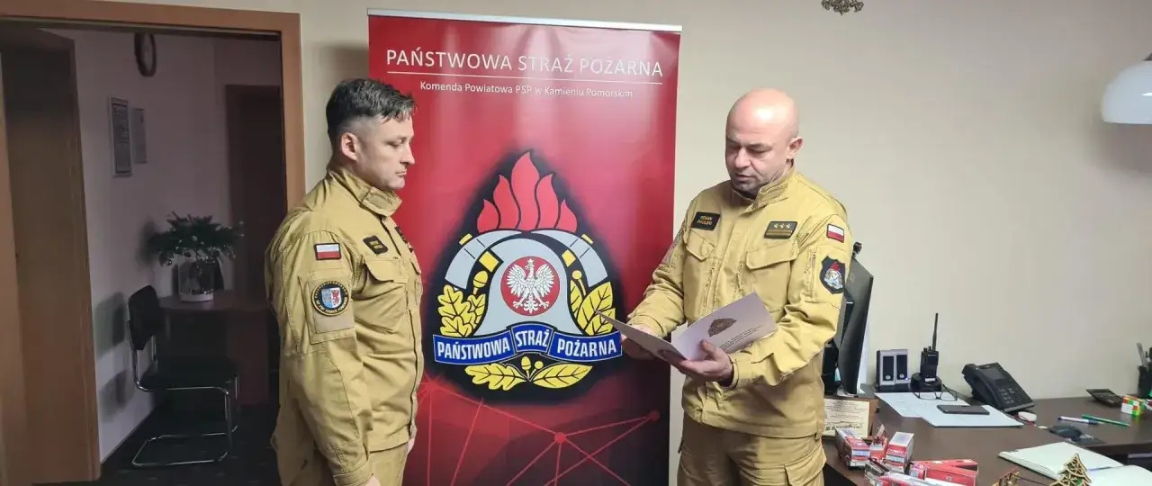 Strażak odbiera gratulacje z okazji jubileuszu 30 lat pracy. Na mundurze widnieje godło Polski i symbol PSP.