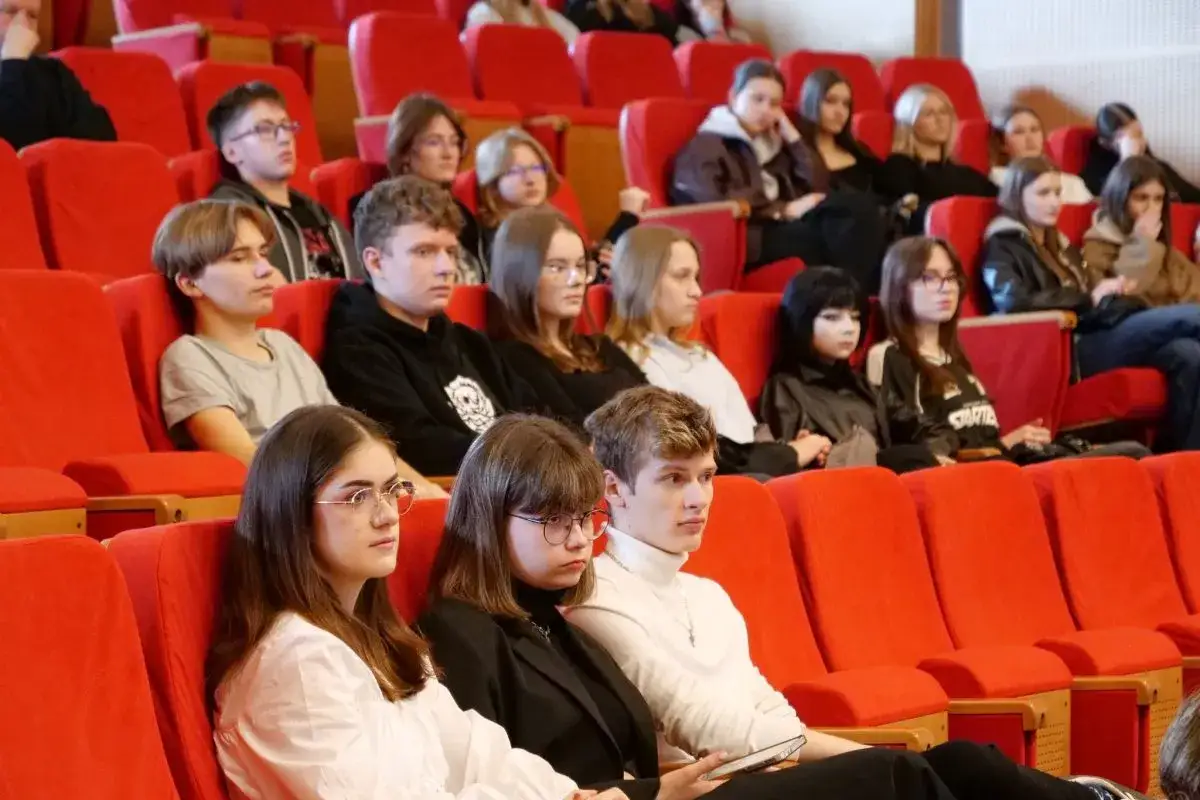 Młodzi ludzie siedzą w czerwonych fotelach, słuchając wykładu. Zastanawiają się, ile trwają studia psychologiczne.