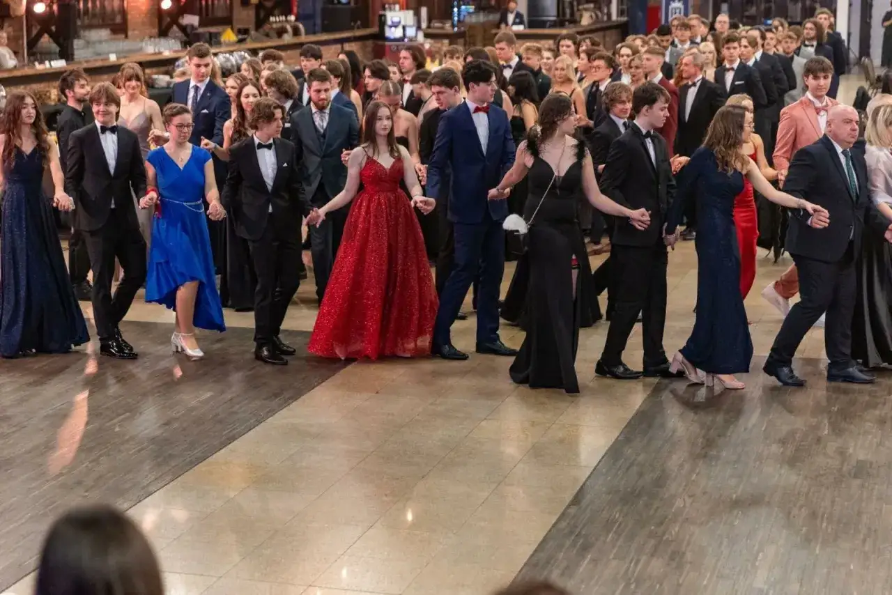 Młodzi ludzie w eleganckich strojach tańczą poloneza na studniówce.