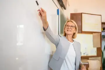 Nauczycielka z markerem przy tablicy, uśmiechnięta. To może być ocena pracy nauczyciela początkującego.