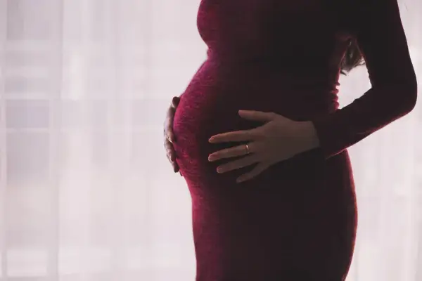 Kobieta w ciąży, z dłońmi na brzuchu, w ciemnoczerwonej sukience. Myśli o zasiłku macierzyńskim po ustaniu zatrudnienia.