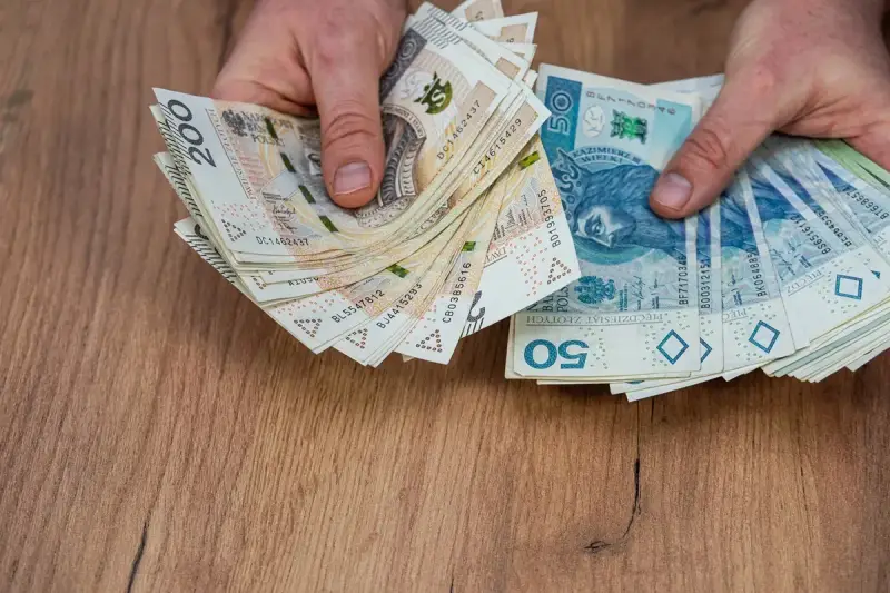 Dłonie trzymające stosy polskich banknotów 200 zł i 50 zł, być może na sześciomiesięczną odprawę emerytalną.